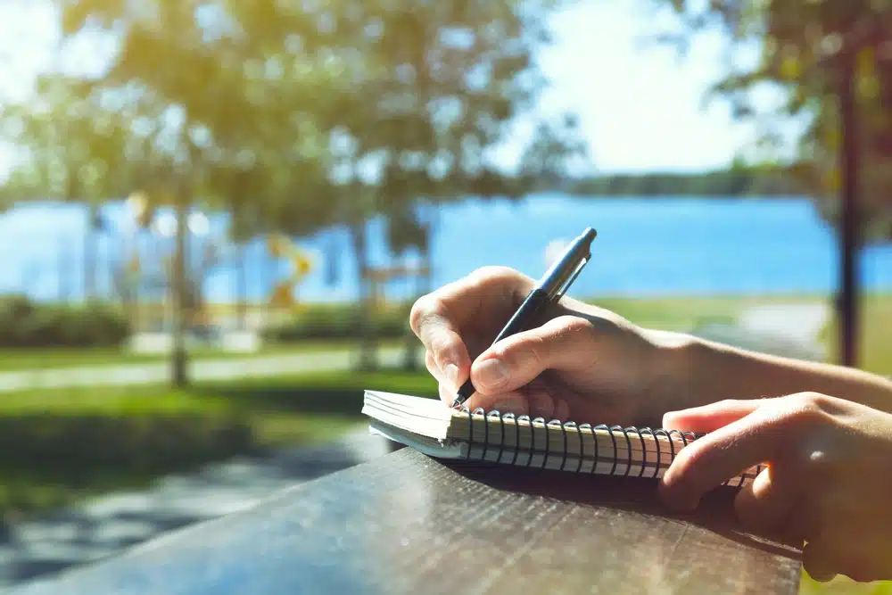 close up of hands writing in a notebook at a park