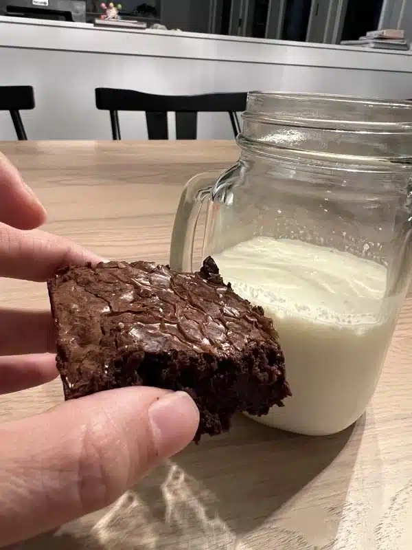 hand holding one einkorn brownie with a glass of milk in background