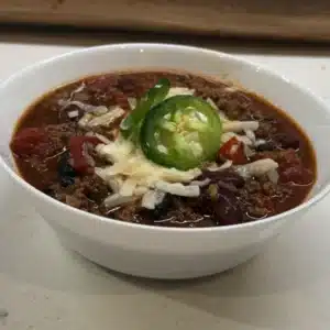 close up of chunky chili recipe with toppings in a white bowl