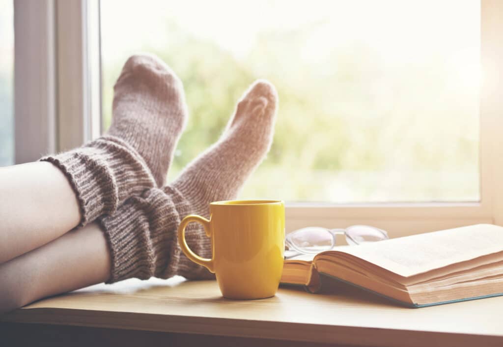 feet on windowsill with hot beverage and book