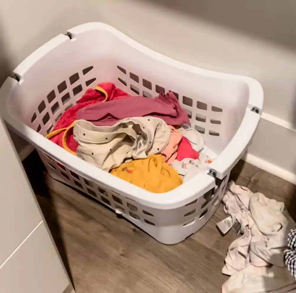 white laundry basket in closet corner with small amount of kid's dirty laundry inside