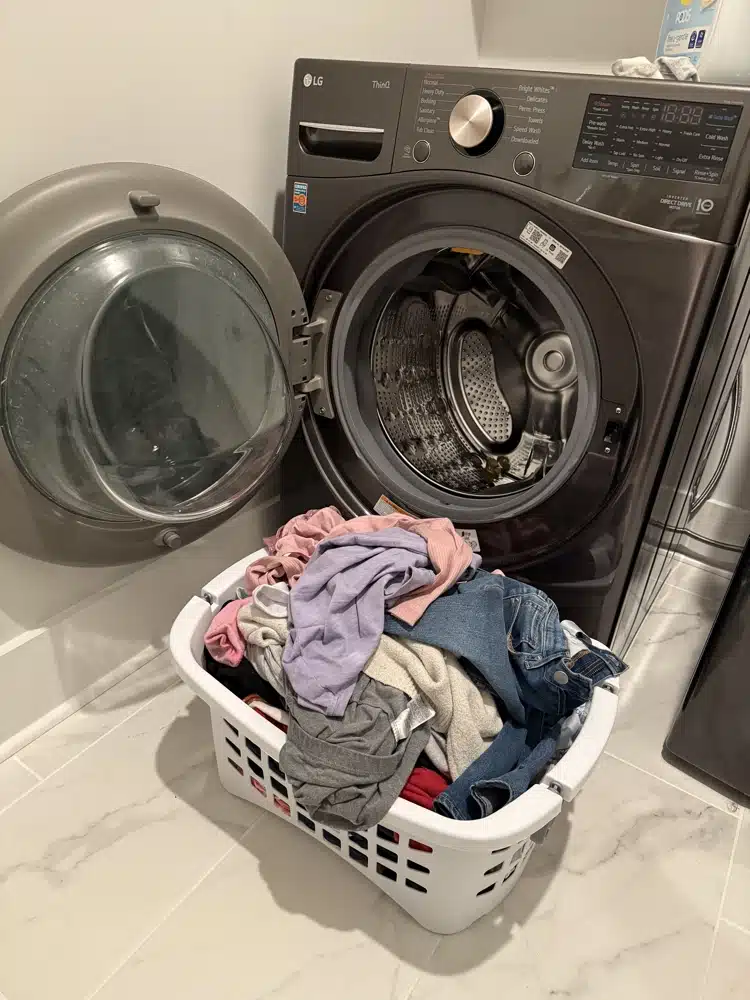 full laundry basket sitting in front of open front-load washer