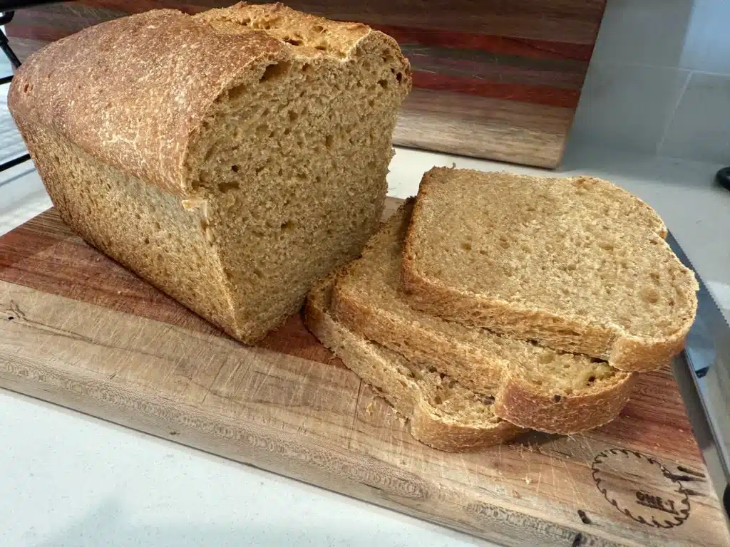 fresh milled sourdough sandwich loaf partially cut on wood cutting board
