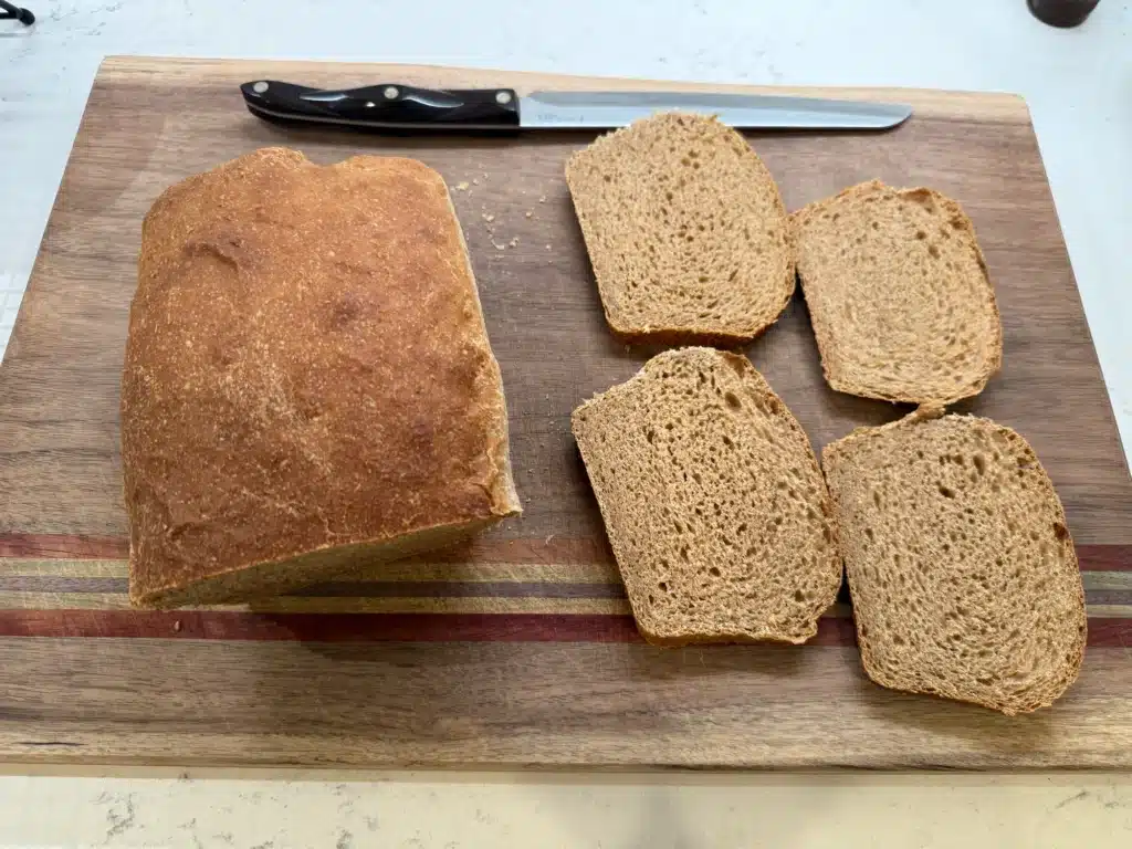 fresh milled sourdough sandwich loaf partially cut on wood cutting board - overhead shot