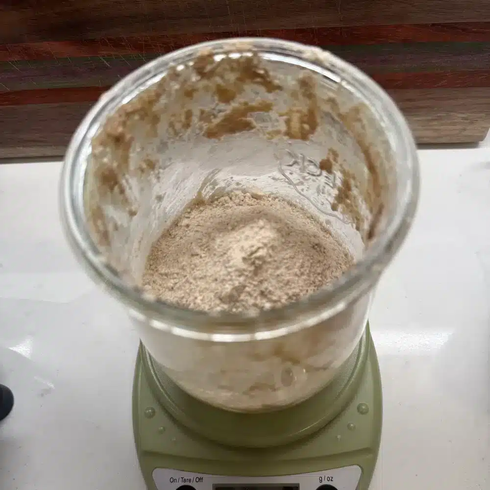 feeding sourdough starter in a Weck jar on a green digital kitchen scale - measuring the flour