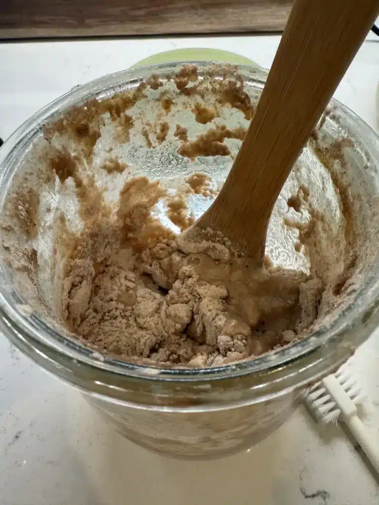 stirring sourdough starter that has just been fed with a long wooden spoon